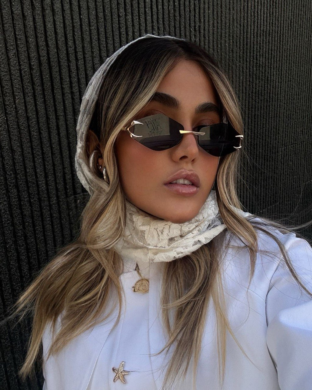 Person wearing sunglasses and a white outfit with a textured background